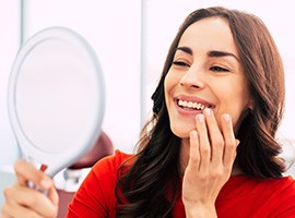 Woman with long brown hair touching teeth while smiling at reflection in mirror