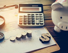A calculator, magnifying glass, piggy bank, and coin stacks on a desk