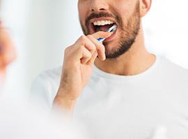 Nose-down view of man in white t-shirt brushing teeth at mirror