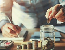 Man dropping a coin into a jar that’s next to multiple coin stacks