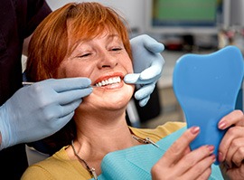 Woman in dental chair smiling at reflection with dentist touching her grin