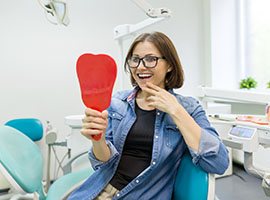 Young woman with glasses checking her smile with dental implants