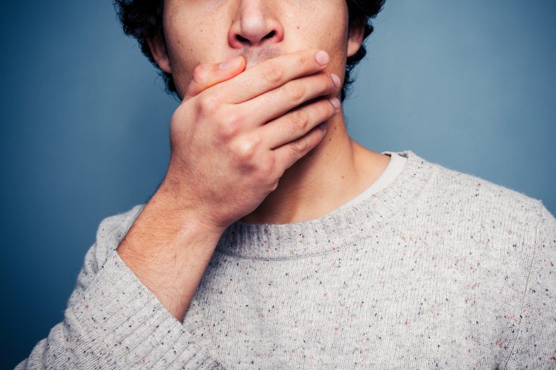 A man with a loose tooth covering his mouth