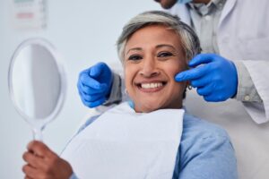 Woman smiling while holding up mirror with dentist in background.