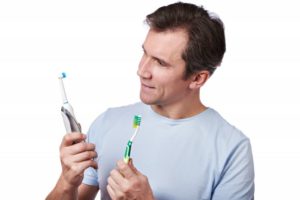 A man comparing an electric and manual toothbrush. 