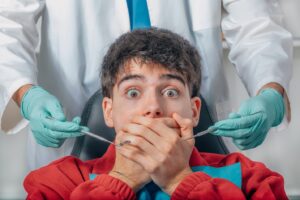 Patient in dentist’s chair covering his mouth with fearful expression.